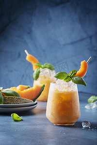 夏季美食西瓜摄影照片_酒吧概念。甜甜的夏季酒，带有甜瓜、冰块和罗勒的蓝色底色。带有文本复制空间的选择性焦点图像