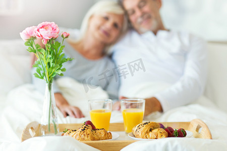 高级夫妇享受早餐躺在床上