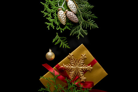 圣诞摄影照片_金光闪闪的圣诞装饰、绿色的thuja枝条和装在黑色上的礼品盒的顶视图
