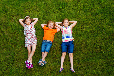 boy摄影照片_Happy children having fun outdoors. Kids playing in summer park. Little boy and two girls laying on green fresh grass