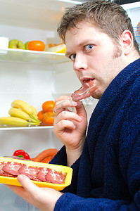 火腿片摄影照片_英俊的男人吃火腿片附近打开冰箱