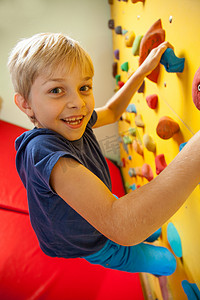 儿童爬山摄影照片_快乐的男孩在攀岩墙上 
