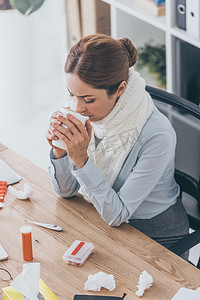 高视角的病态女实业家在围巾坐在办公室喝茶