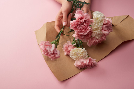裁剪拍摄的妇女包裹美丽的花朵在工艺纸粉红色
