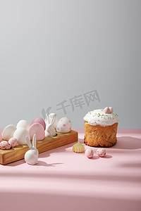 复活节彩蛋放在木制木板上，旁边有装饰兔子，靠近粉色和灰色背景的复活节蛋糕