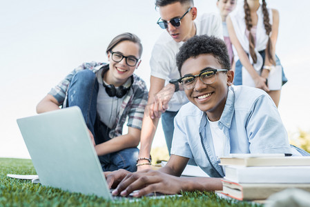 快乐的多民族青少年使用笔记本电脑和在公园学习 