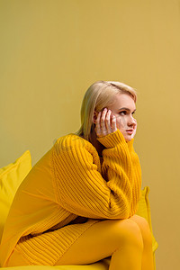 黄色毛衣和紧身衣的年轻金发女郎的侧面看黄色沙发上