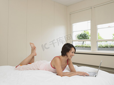 躺着的人像摄影照片_使用笔记本电脑的睡衣的女人