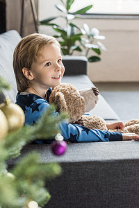可爱的微笑的孩子抱着泰迪熊和坐在沙发侧面视图
