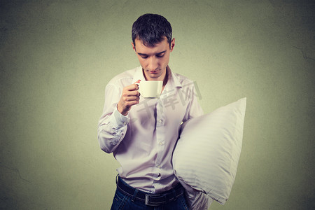 pillow摄影照片_very tired, almost falling asleep business man holding a cup of coffee and pillow 