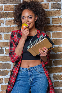 非洲裔美国女孩吃苹果和控股笔记本同时看着相机
