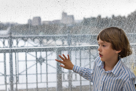可爱的男孩站在一个潮湿的窗口