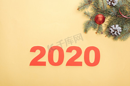 2020圣诞新年摄影照片_靠近黄底有灌木和球果的圣诞树枝的2020年纸牌号顶部视图