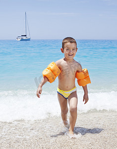 小男孩穿着橙色充气臂章的海滩上运行