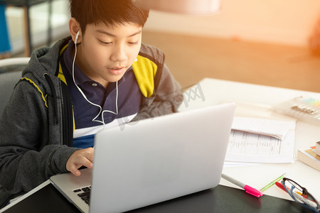 亚洲逗人喜爱的男孩使用笔记本电脑与阳光在早晨在家.