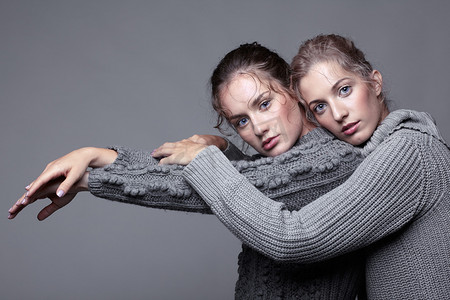 两个点摄影照片_灰色背景的灰色毛衣两个年轻的妇女。美丽的 g