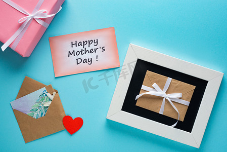 抽奖设计摄影照片_有快乐妈妈的礼品盒、信封和贺卡的顶部视图，用蓝色背景写上一天的字母
