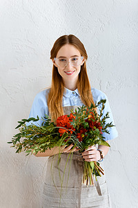 美丽的年轻花店在眼镜抓紧花花束和微笑在照相机