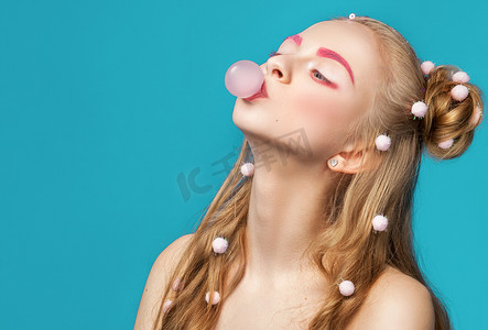 时尚流行发型摄影照片_年轻美丽和有趣的女人粉红色泡泡糖吹过蓝光