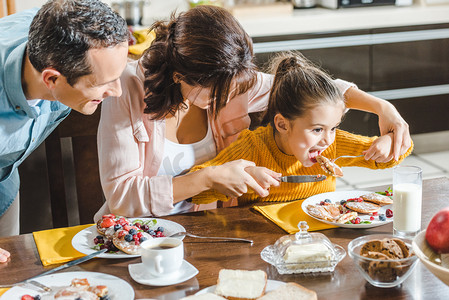 愉快的家庭一起吃薄饼与莓果在桌, 母亲哺养的女儿