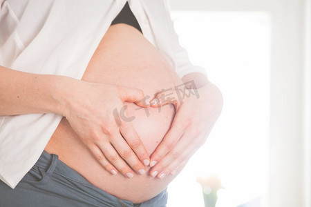 怀孕的女孩牵手心在家的肚子的形状