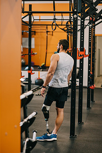运动年轻的运动员与人工腿站在体操梯子附近在健身房
