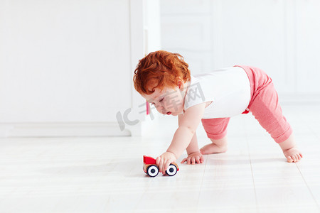 可爱的红发男婴滚动在地板上的一辆玩具车