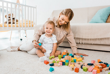 可爱的幼儿玩五颜六色的立方体和母亲在托儿所室