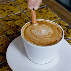 cappucino摄影照片_一杯咖啡拿铁咖啡被搅动的肉桂棒.