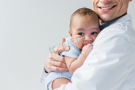 小博士摄影照片_裁剪拍摄的微笑儿科医生抱着小婴儿在白色隔离