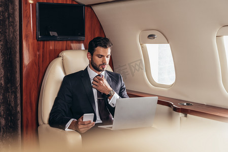 免vip摄影照片_穿着西服的商人使用笔记本电脑和私人飞机上的智能手机的选择性焦点 