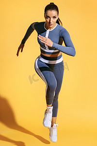 美丽的妇女赛跑者在剪影在黄色背景。运动妇女的相片在时尚运动服。动态运动。力量和动力。全长