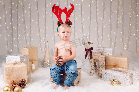 新年摄影照片_白色高加索孩子的画像鹿麋垫铁头巾庆祝圣诞节或新年。小可爱的男孩在演播室与冬天假日装饰