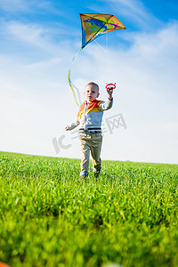 年轻男孩玩耍着他的风筝在绿色的原野.