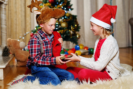 圣诞孩子们摄影照片_在圣诞帽子和女孩认为礼物男孩