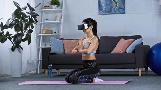身穿运动服，头戴耳机的年轻女子坐在健身垫上在家锻炼