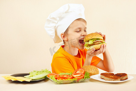 在厨师的帽子微笑的小男孩吃煮熟的汉堡