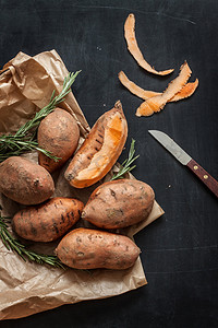 黑色美食海报摄影照片_Peeling sweet potatoes with knife on black chalkboard