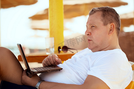 男人应酬摄影照片_男人带着便携式计算机在海滩度假村放松