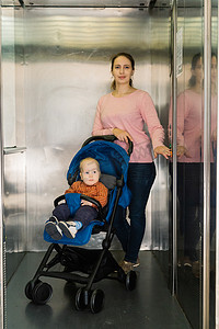 电梯乘坐摄影照片_在商场里, 妇女带着一个婴儿乘坐电梯.