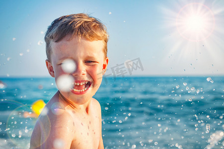 幸福的男孩沐浴，在海水溅上阳光灿烂的日子。白种人的孩子做飞溅与水珠。暑假在海上。海滩上的孩子。度假概念