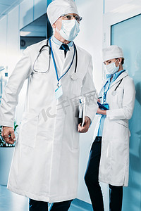 医用口罩男医生与数码片同行当他的女同事站在医院走廊的剪贴板后面 