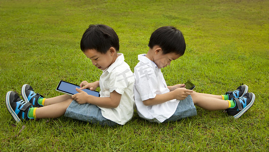 使用電腦摄影照片_两个孩子使用的触摸屏平板电脑在草地上