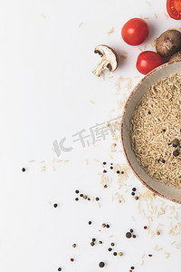 原始大米和香料在碗与蘑菇和蕃茄在白色表面与拷贝空间的顶面看法