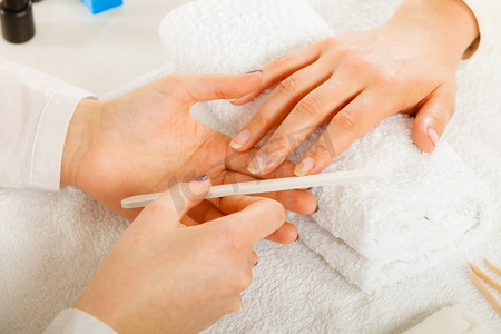 纵容摄影照片_女人的手放在毛巾上，美容师锉指甲。美容养生水疗护理，美甲概念。妇女得到美甲做文件指甲
