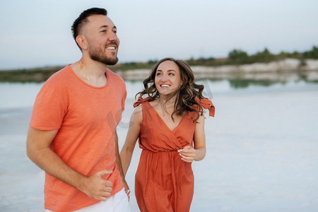 一对穿着橙色衣服的年轻夫妇带着狗在空荡荡的沙滩上