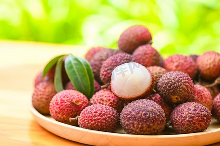 吃荔枝摄影照片_在热带水果泰国夏季，木盘背景上的绿叶荔枝水果，新鲜的成熟荔枝从荔枝树上剥下来