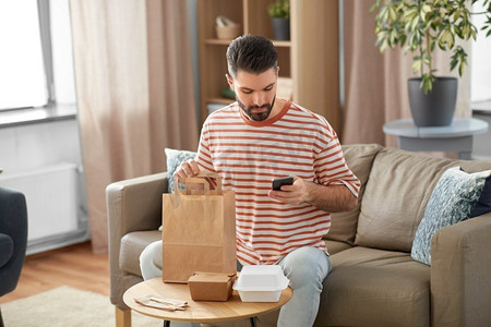 沟通、休闲和人际概念—男子在家中使用智能手机进行外卖订购检查。一名男子用电话检查家中的食品订单