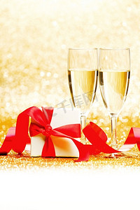 2018狗年金色中国风摄影照片_香槟酒杯，白色盒子，金色背景上有红色丝带。香槟和礼物