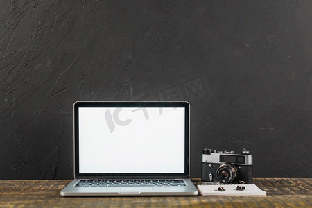 有空白屏幕膝上型计算机复古相机黑色背景的木桌子